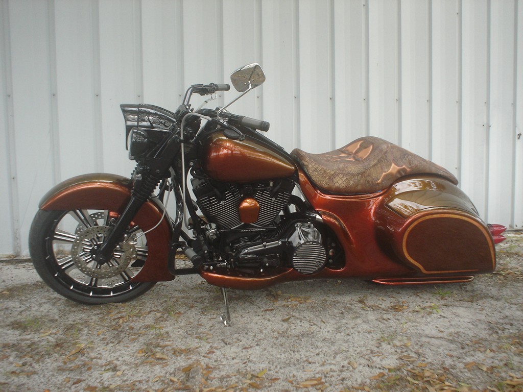 A copper bagger with a hand-tooled leather seat and matching tooled panels, parked by a metal shop wall